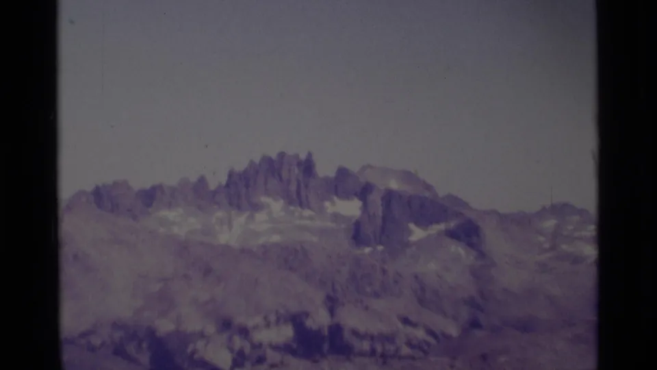 A 1975 home-movie frame shows the Minaret Wilderness landscape from a distance, with sharp rocky spires and snow remnants softened by 8mm color shift.