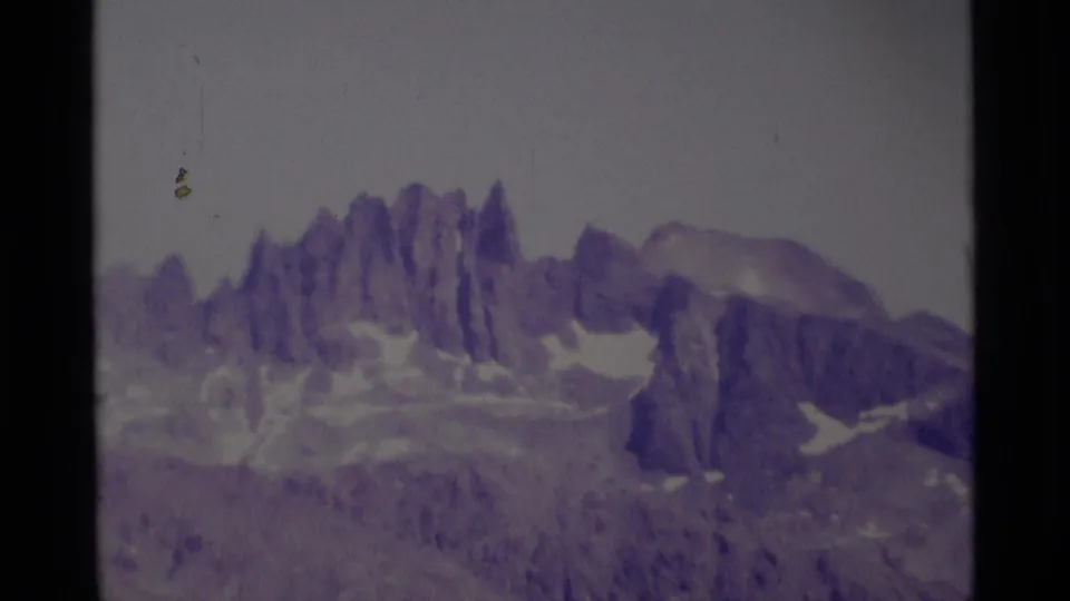 The zoom brings the Minaret Wilderness peaks closer, emphasizing jagged rock formations, snow pockets, and muted purple 8mm film color.