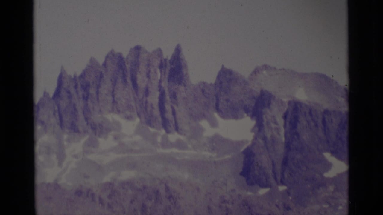 1975 8mm view of jagged Minaret Wilderness peaks with snow patches and a faded purple film cast.