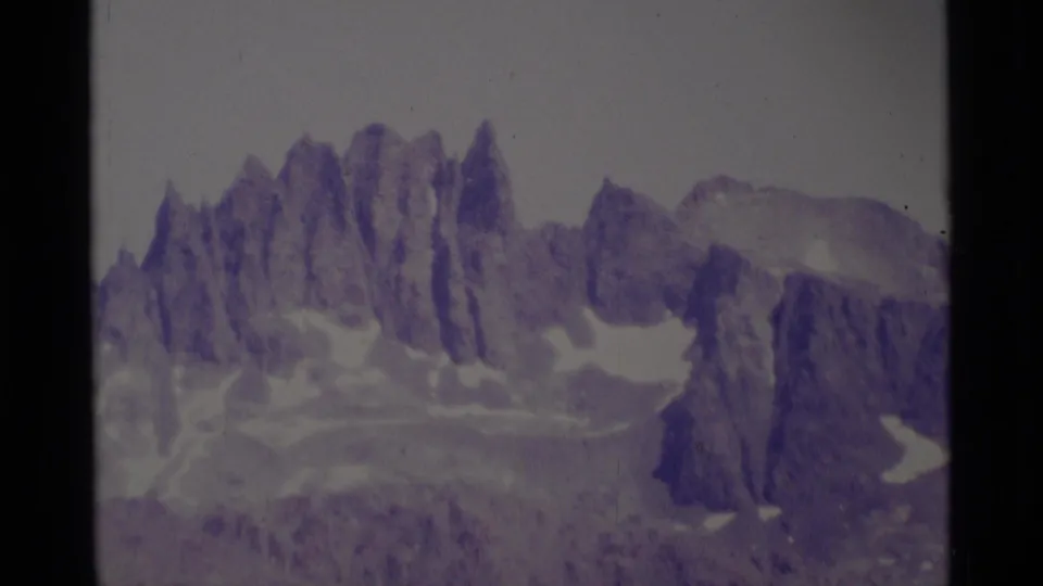 1975 8mm view of jagged Minaret Wilderness peaks with snow patches and a faded purple film cast.