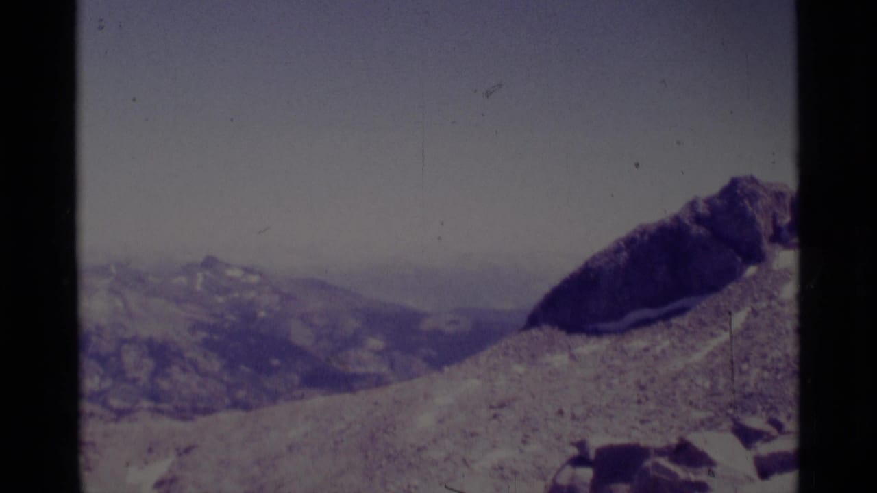 Rocky mountain slope with a dark ridge at right and distant hazy ranges.