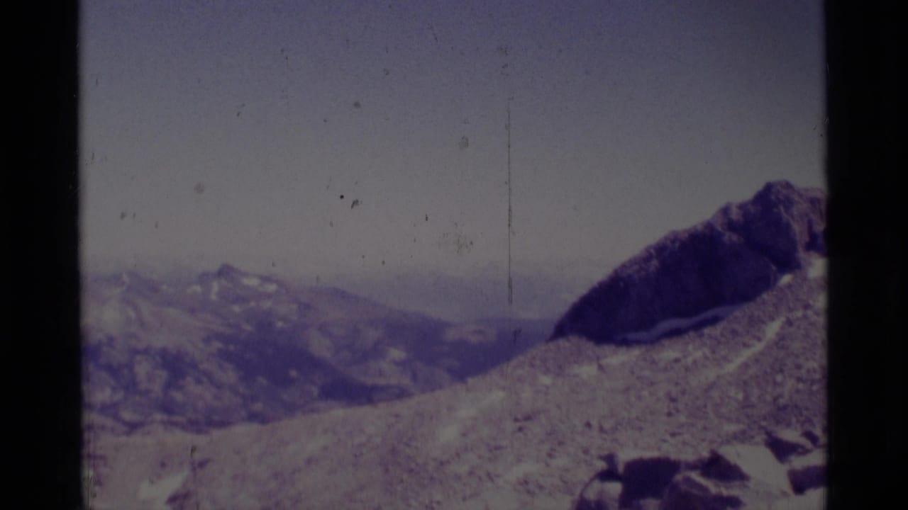 1975 8mm Minaret Wilderness view of rocky high-elevation terrain, distant ridgelines, and patches of snow under a pale sky.