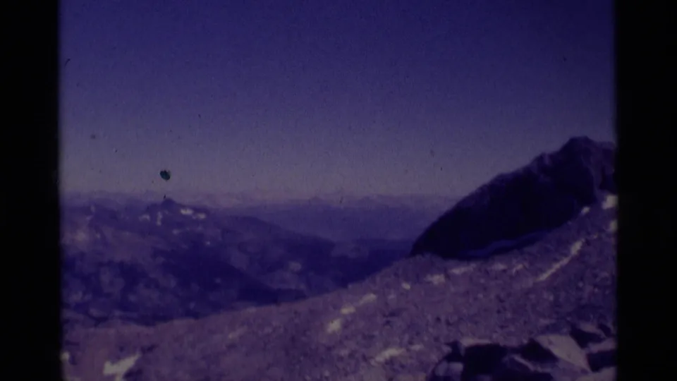 1975 8mm view across Minaret Wilderness terrain, with a dark rocky peak, distant ridges, snow patches, and visible film dust.