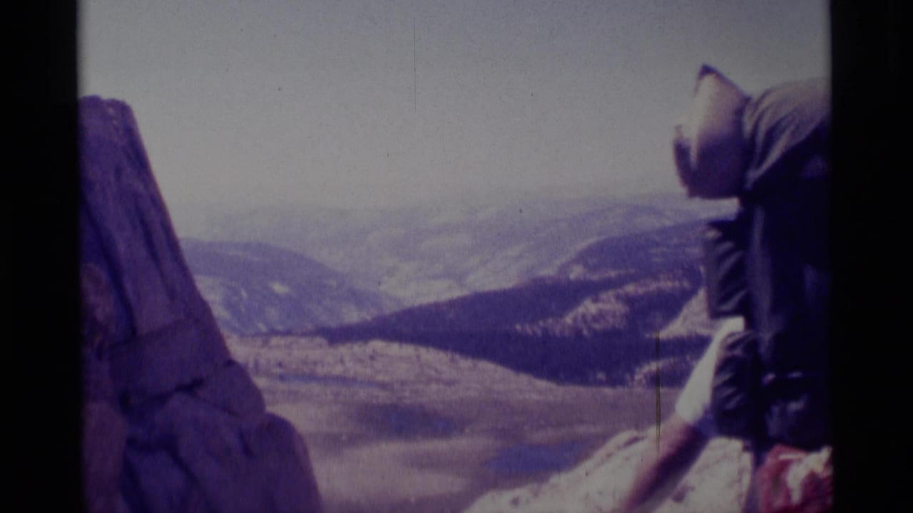 1975 8mm frame from Minaret Wilderness showing a hiker with a large pack near rock above a distant mountain valley.