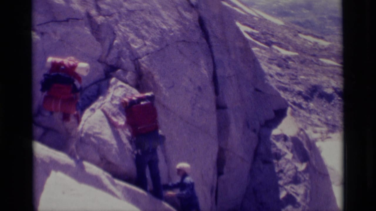Backpackers in the Minaret Wilderness area appear to negotiate a sloped rock ledge with large packs in 1975 8mm footage.