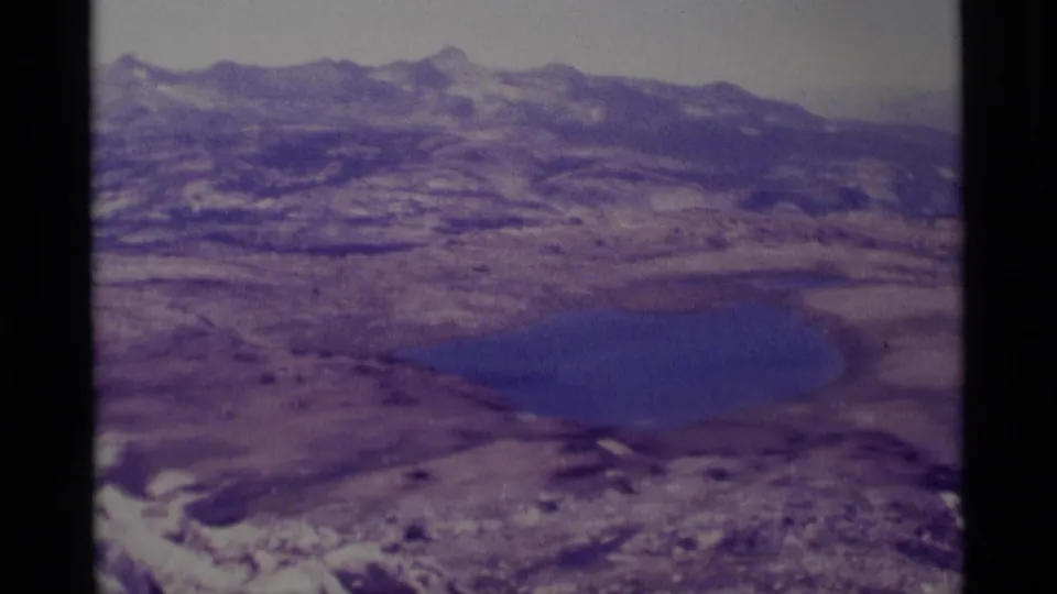 1975 8mm wilderness panorama of a blue alpine lake below rugged Minaret Wilderness ridges and rocky high-country terrain.