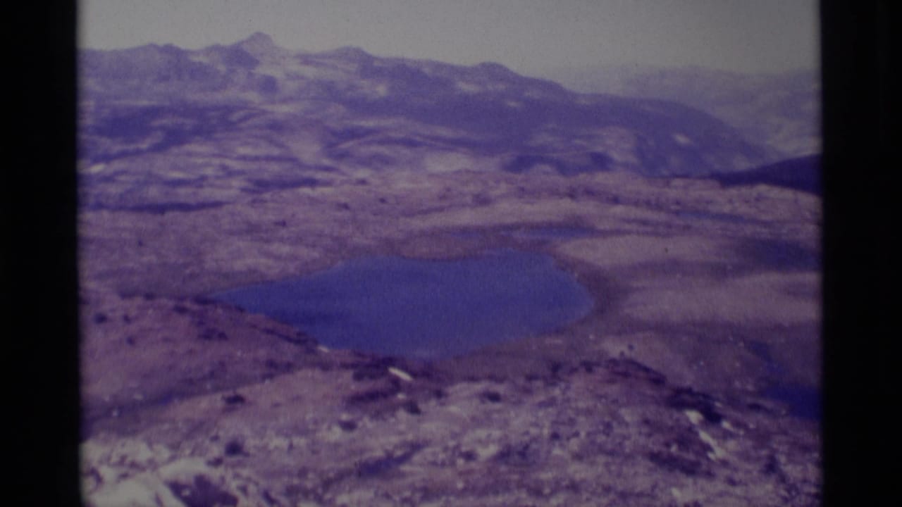 1975 8mm view of a blue lake and rugged peaks in the Minaret Wilderness area, seen from an elevated rocky vantage.