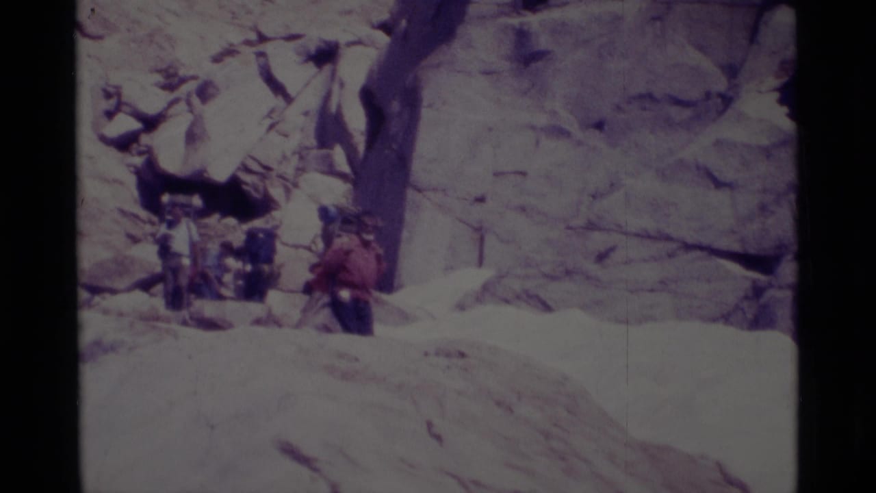 In the Minaret Wilderness, backpackers with large packs move carefully down a bright rocky slope in 1975 home-movie footage.