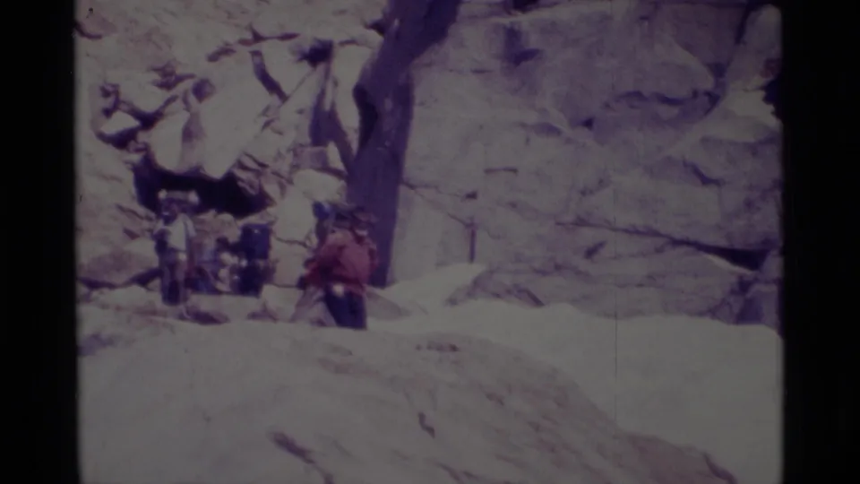 In the Minaret Wilderness, backpackers with large packs move carefully down a bright rocky slope in 1975 home-movie footage.