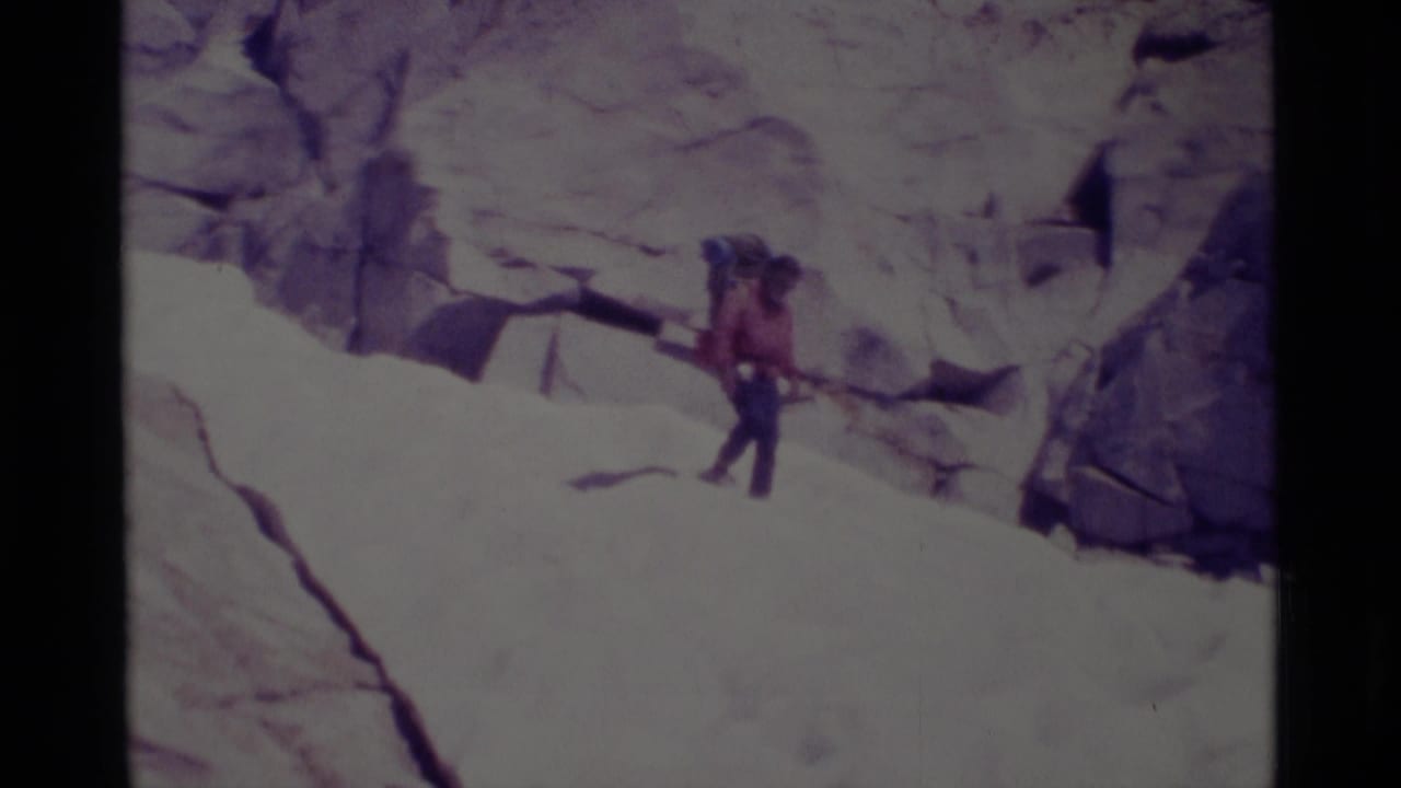 A hiker with a large pack walks across a sloped granite surface.