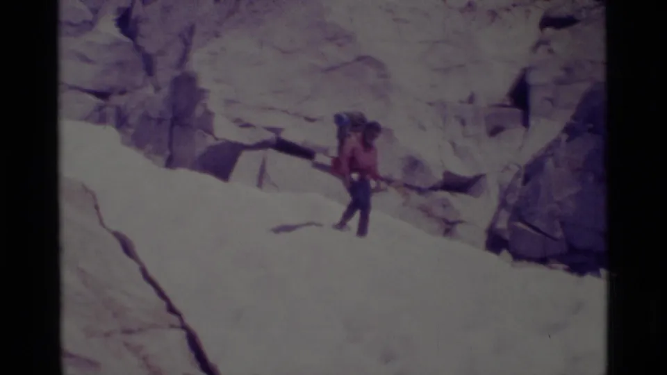 A backpacker crosses a sunlit rocky slope in Minaret Wilderness, with granite walls filling the background.