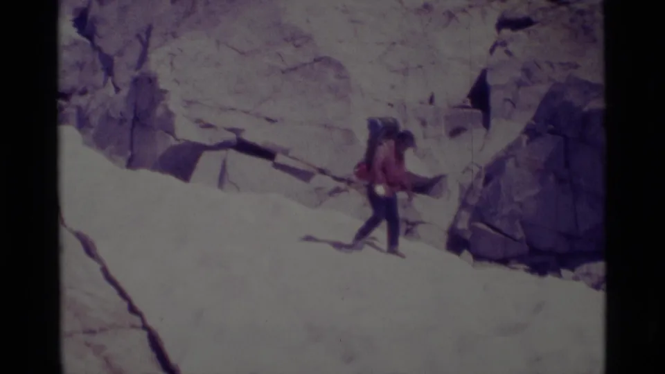 The 1975 8mm frame shows a backpacked hiker descending pale granite terrain in the Minaret Wilderness.
