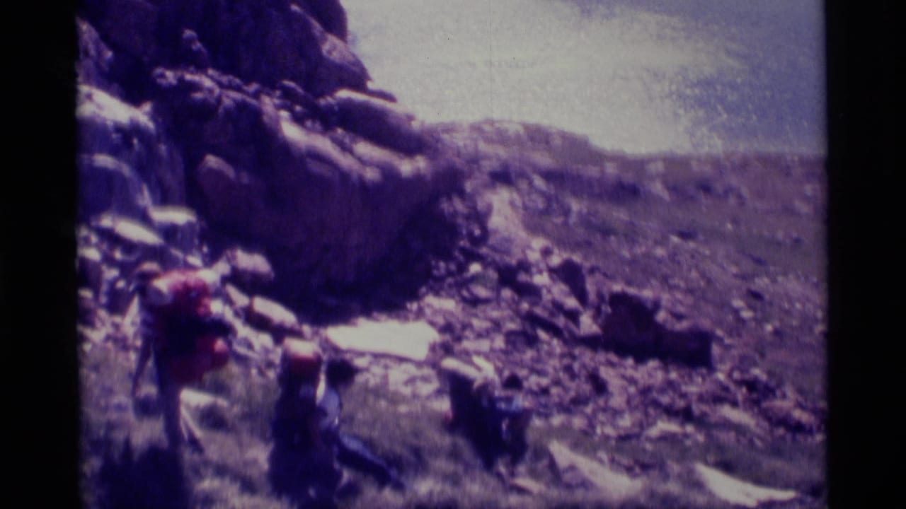 1975 8mm home-movie frame of hikers on dark rocks near a calm lake in the Minaret Wilderness area.
