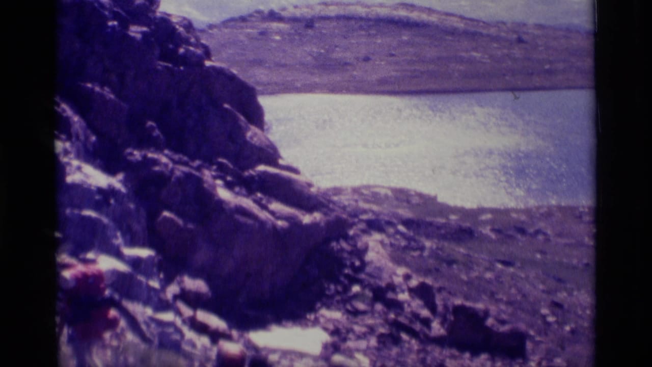 Rocky shoreline and calm lake with distant hills beyond.