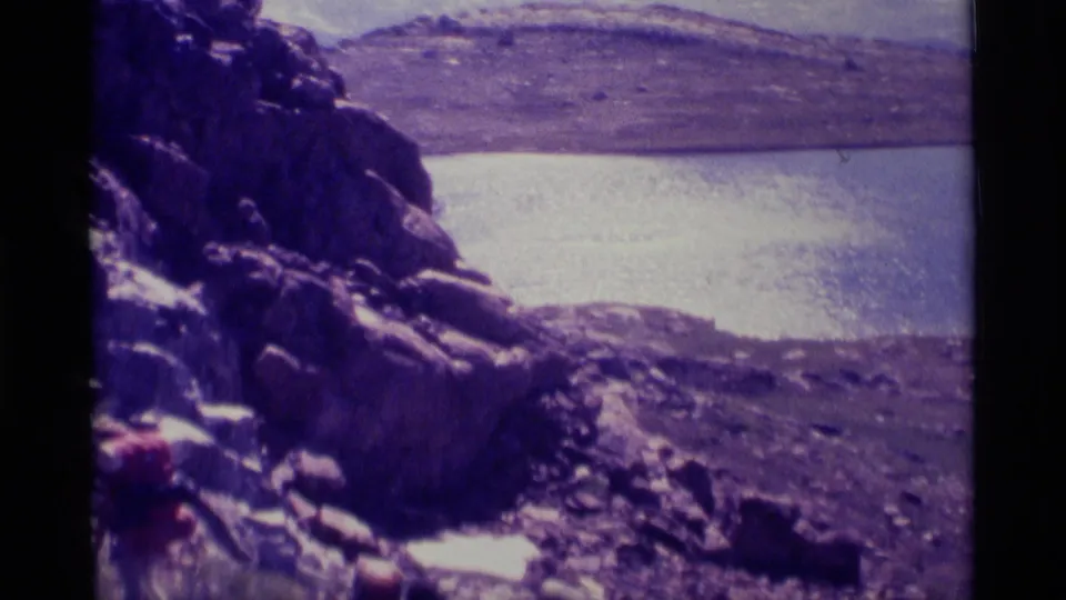 Handheld 8mm view across shoreline rocks, lake water, and distant mountain slopes in California wilderness.