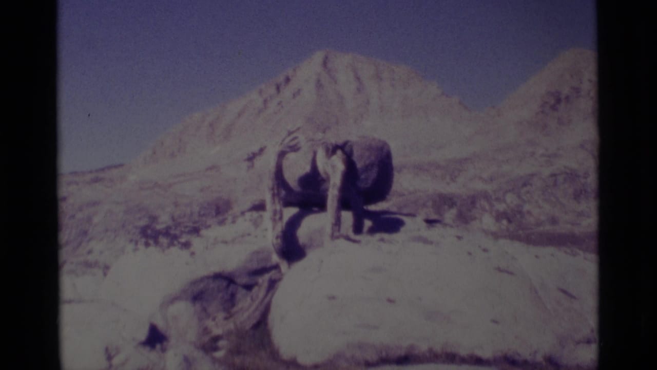 Outdoor sculpture on rock with a broad mountain slope in the background.