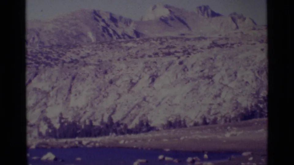 Wide 1975 8mm view of rocky Minaret Wilderness terrain, a small lake, and distant mountain slopes.