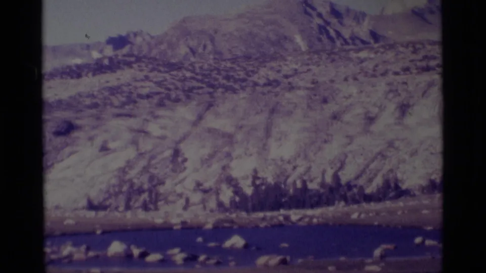 Faded 8mm Minaret Wilderness frame looking over a small lake toward rocky alpine hills and pale mountain slopes.