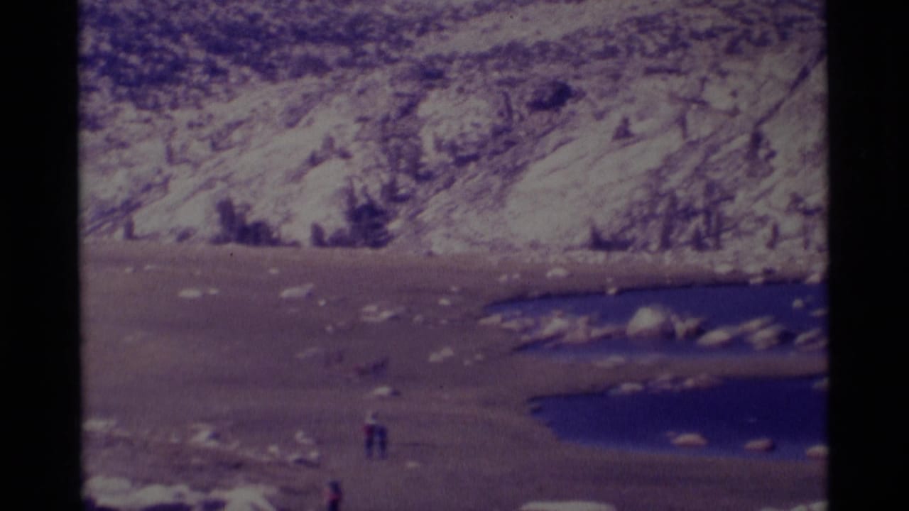 Distant hikers cross an open lakeside plain beneath rocky Minaret Wilderness slopes in 1975 8mm footage.