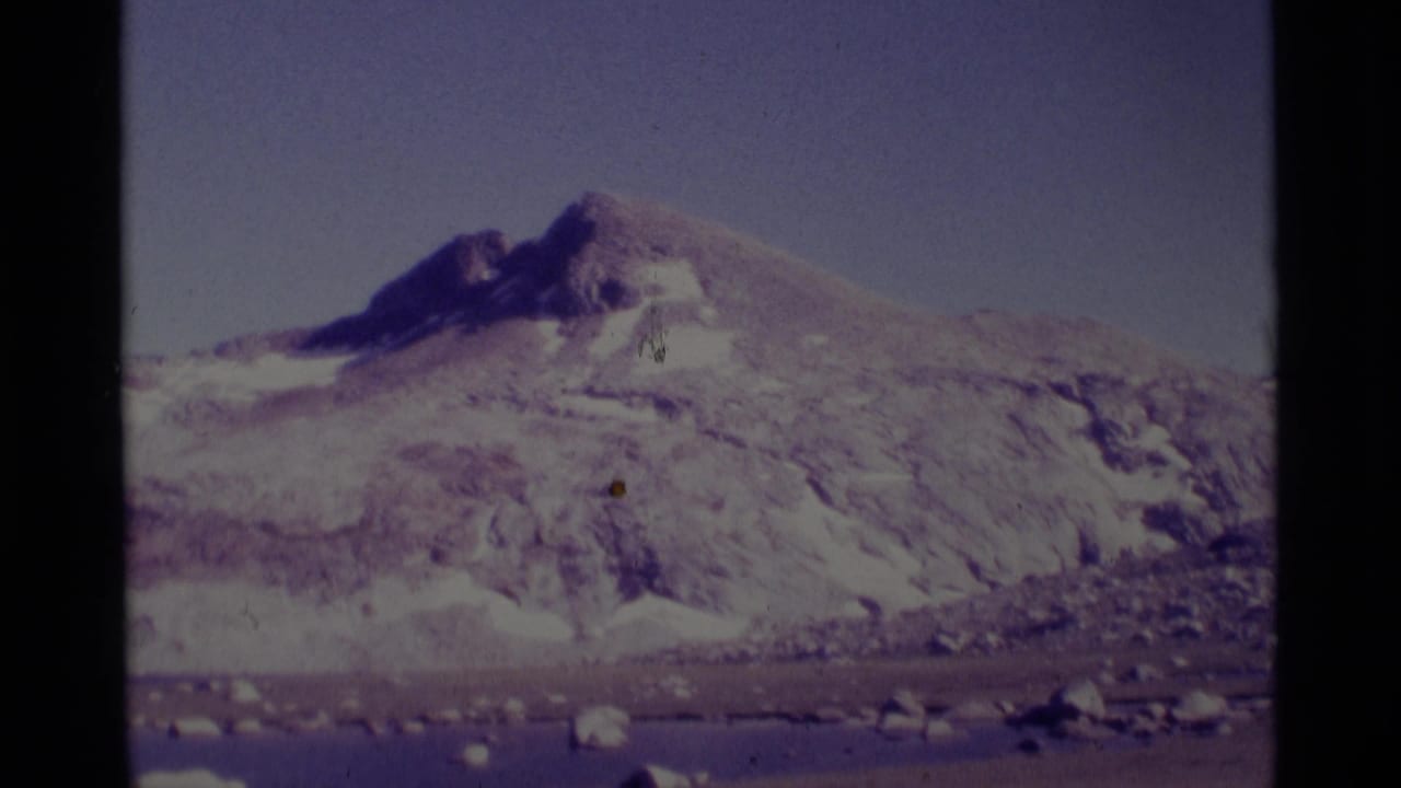 Distant snow-streaked mountain peak and rocky slope seen through 8mm frame borders.