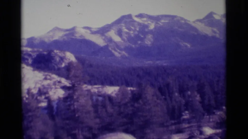 1975 8mm view across a pine-covered valley toward snow-capped mountain ridges in the Minaret Wilderness area.