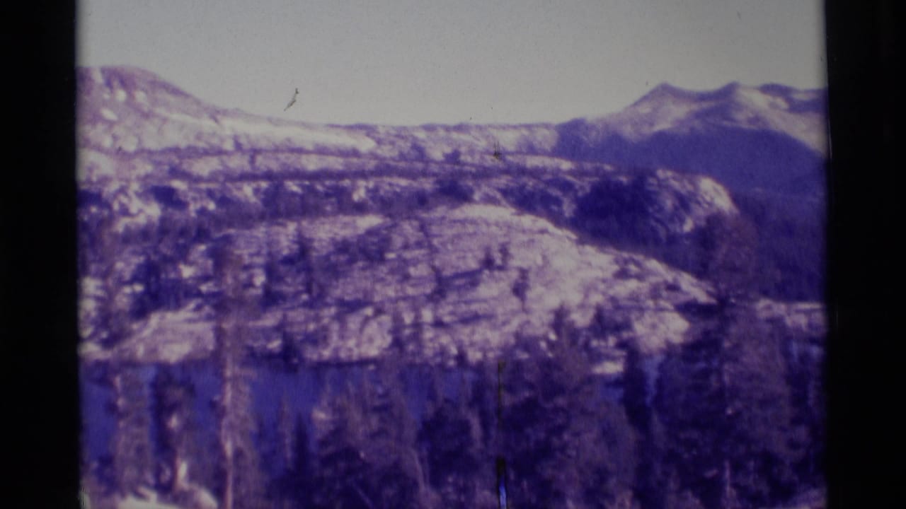 1975 8mm view of the Minaret Wilderness area, showing a snow-dusted ridge, forested slopes, and rocky high-country terrain.