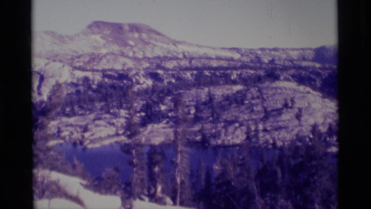 Minaret Wilderness landscape with an alpine lake, evergreen forest, and rugged mountain slopes recorded on 8mm film in 1975.