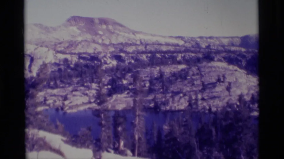 Minaret Wilderness landscape with an alpine lake, evergreen forest, and rugged mountain slopes recorded on 8mm film in 1975.