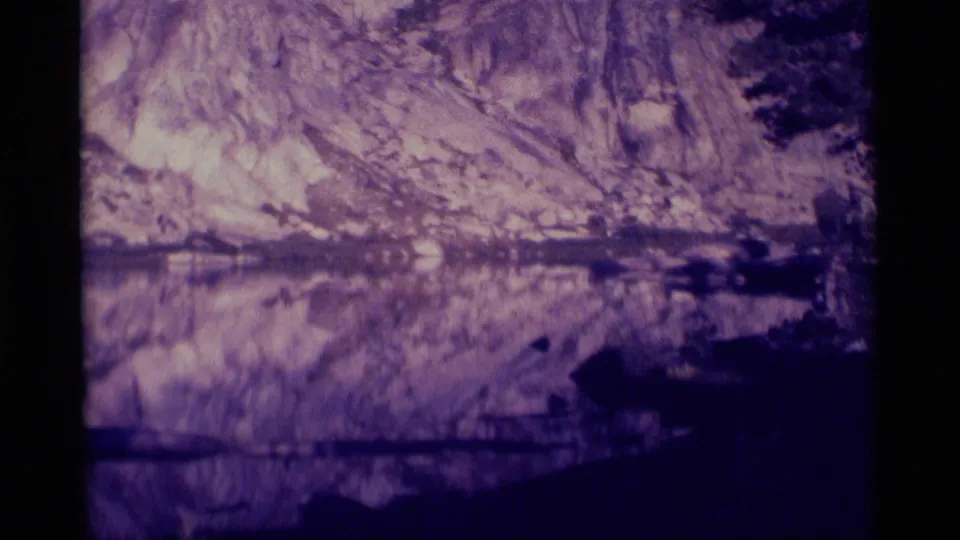 1975 8mm Minaret Wilderness scene with rocky mountain texture reflected in a lake or pond and dark shoreline forms below.