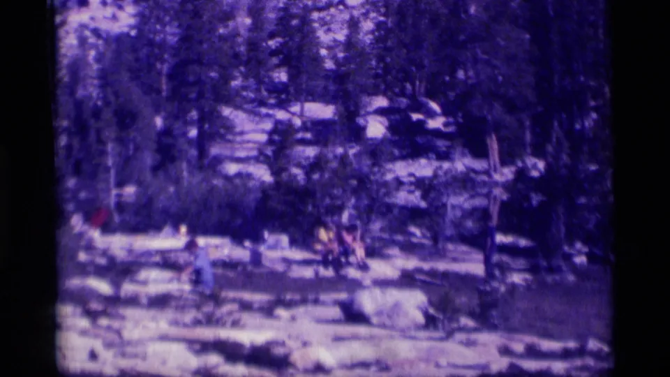 Distant family or group figures appear near boulders and evergreens in the 1975 Minaret Wilderness lake scene.
