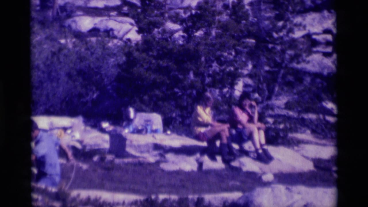 1975 8mm home-movie frame of people resting at a rocky picnic area in the Minaret Wilderness, with trees and stone formations behind them.