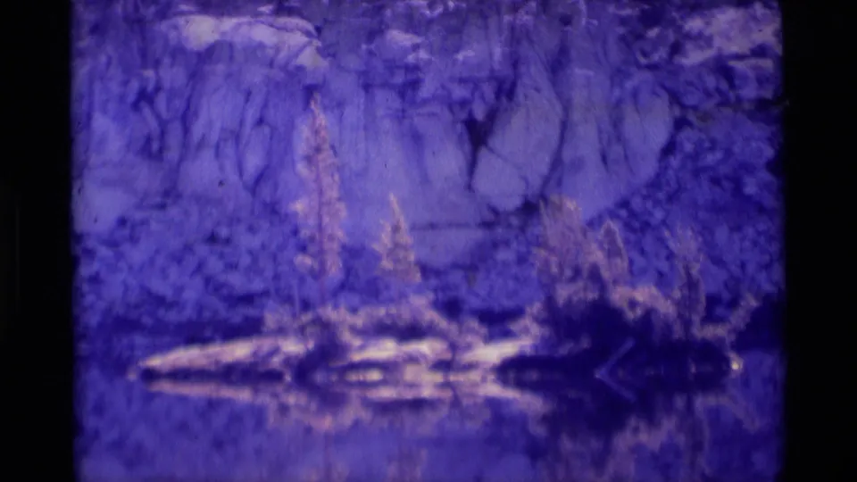 Minaret Wilderness landscape frame showing reflective water or shoreline, low vegetation, pale rock, and the soft grain of 8mm film.