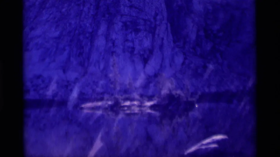 1975 8mm frame of a blue-purple cave or rock interior, with darker horizontal areas and bright marks from film or reflected light.