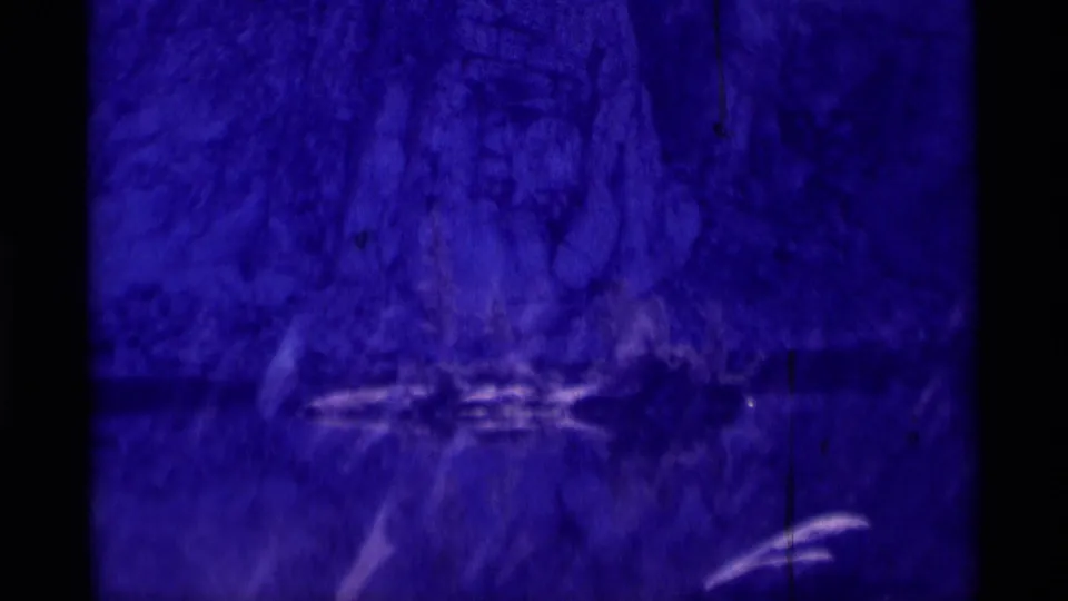 Final Minaret Wilderness 8mm frame holding on a blue-purple cave surface, with vertical film scratches and pale curved streaks near the lower edge.