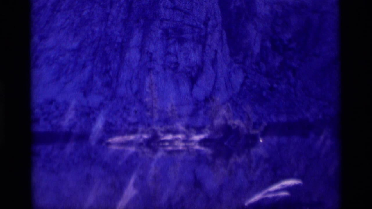 Blue-purple rocky cliff reflected in still water with a dark horizontal waterline.