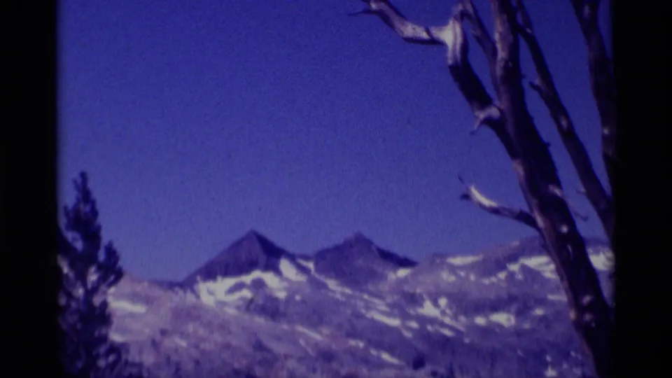 Closer 8mm view of Minaret Wilderness peaks, with snow-streaked ridges and bare branches along the right edge of the frame.