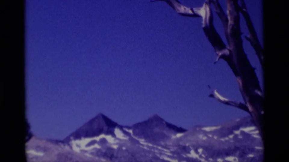 1975 8mm view of snow-streaked peaks in Minaret Wilderness, with a bare tree limb crossing the foreground.