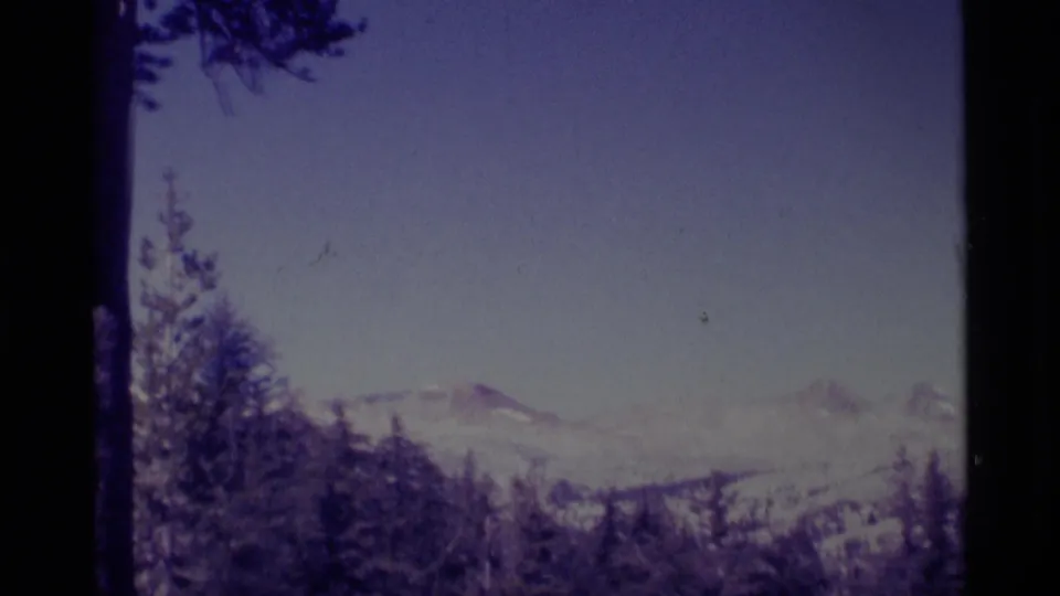 The 1975 8mm footage shows a distant snowy mountain panorama from a wooded California vantage point.