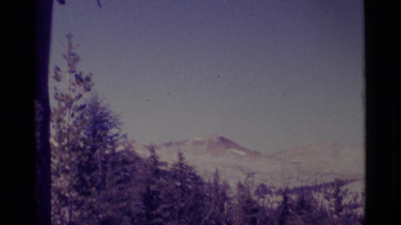Wide mountain vista with trees in the foreground and snow patches on distant ridges.