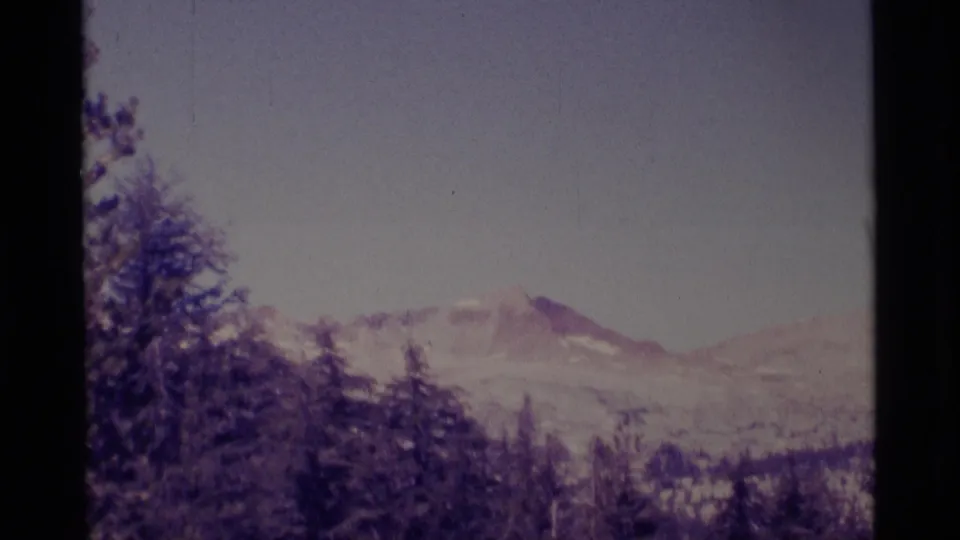1975 California wilderness view with forested slopes below hazy, snow-dusted mountains on small-gauge film.