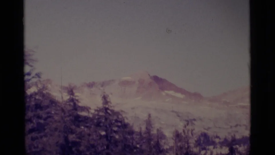 Final 1975 8mm frame of Minaret Wilderness mountains, with dark pines below a snow-streaked ridge and pale sky.