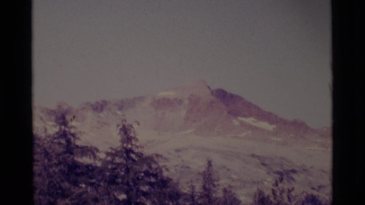Distant California wilderness mountain view with snow patches, conifer silhouettes, soft focus, and visible 8mm frame edges.