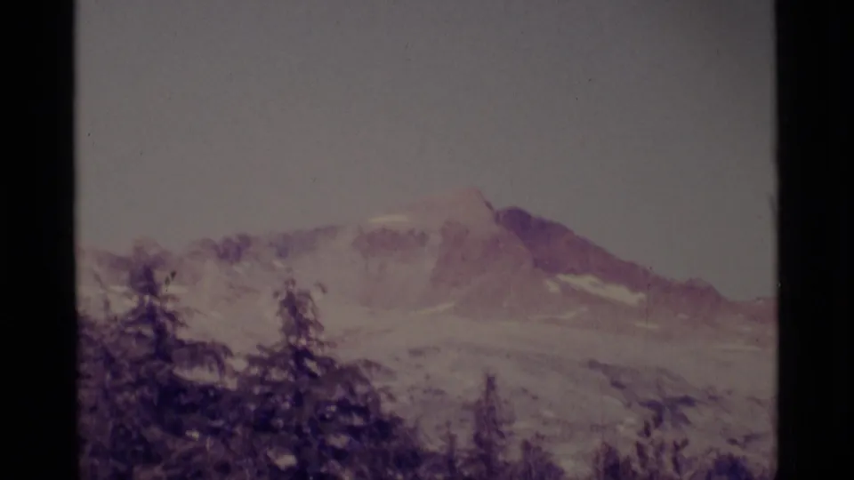 Distant California wilderness mountain view with snow patches, conifer silhouettes, soft focus, and visible 8mm frame edges.