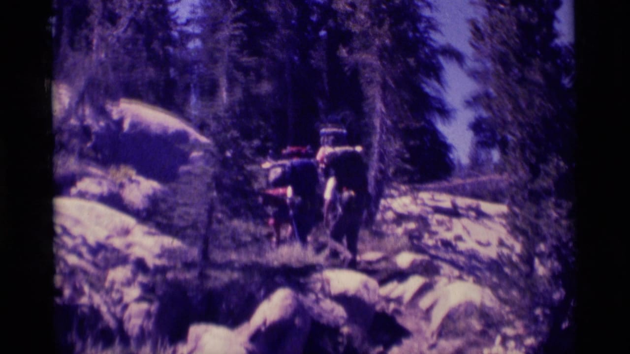 1975 8mm footage shows backpackers on a rocky Minaret Wilderness forest trail under tall trees.