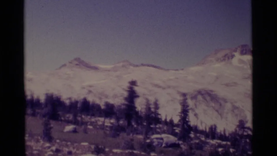 1975 8mm view of the Minaret Wilderness area with distant snowy ridges, pine trees, rocky meadow ground, and soft home-movie exposure.