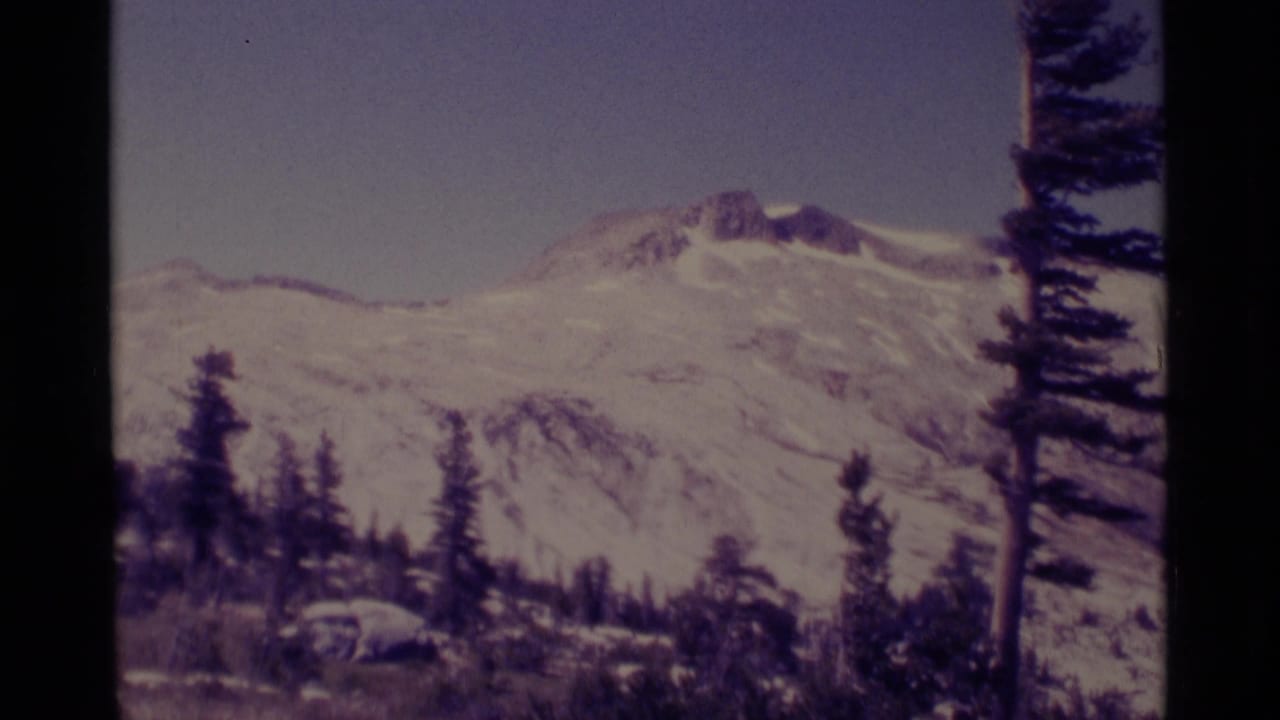 1975 8mm frame of a snowy Minaret Wilderness mountain peak with evergreen silhouettes and visible film gate edges.