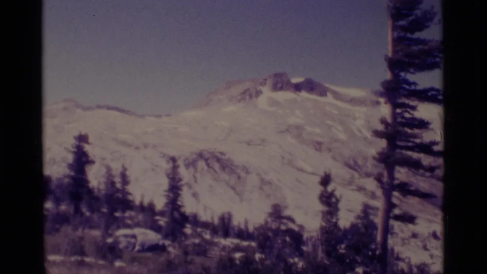 1975 8mm frame of a snowy Minaret Wilderness mountain peak with evergreen silhouettes and visible film gate edges.