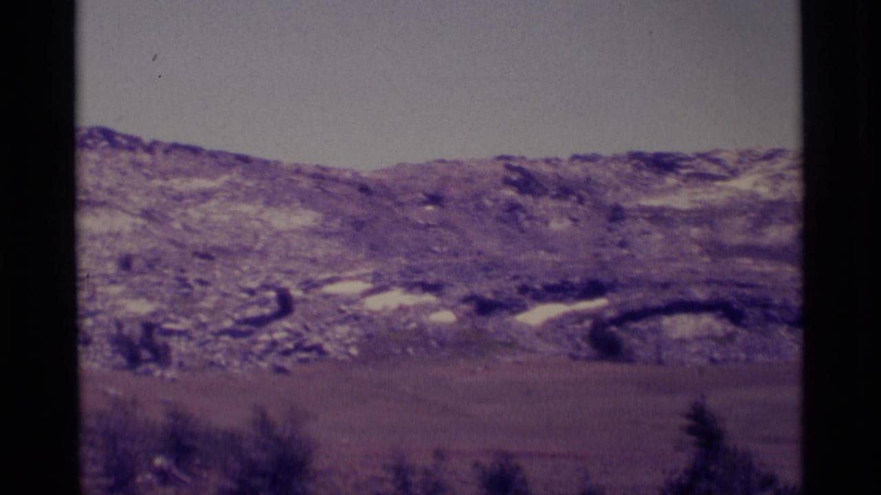 Snow-streaked hills and a broad valley seen through dark film-frame borders.