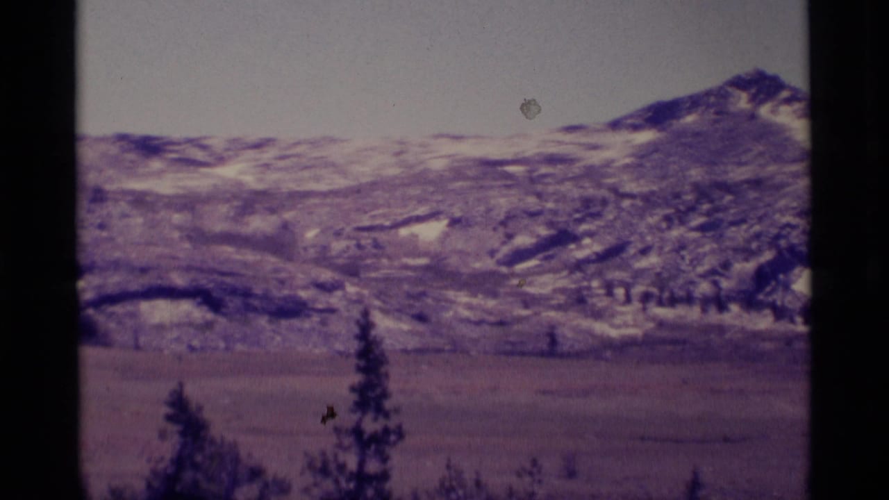 1975 8mm view of Minaret Wilderness mountains, with snow patches on ridges above a broad meadow and conifer silhouettes.