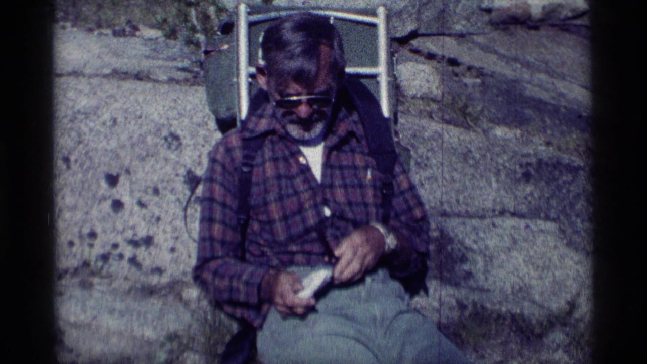 Man in sunglasses sits on a rock with a pipe and backpack behind him.